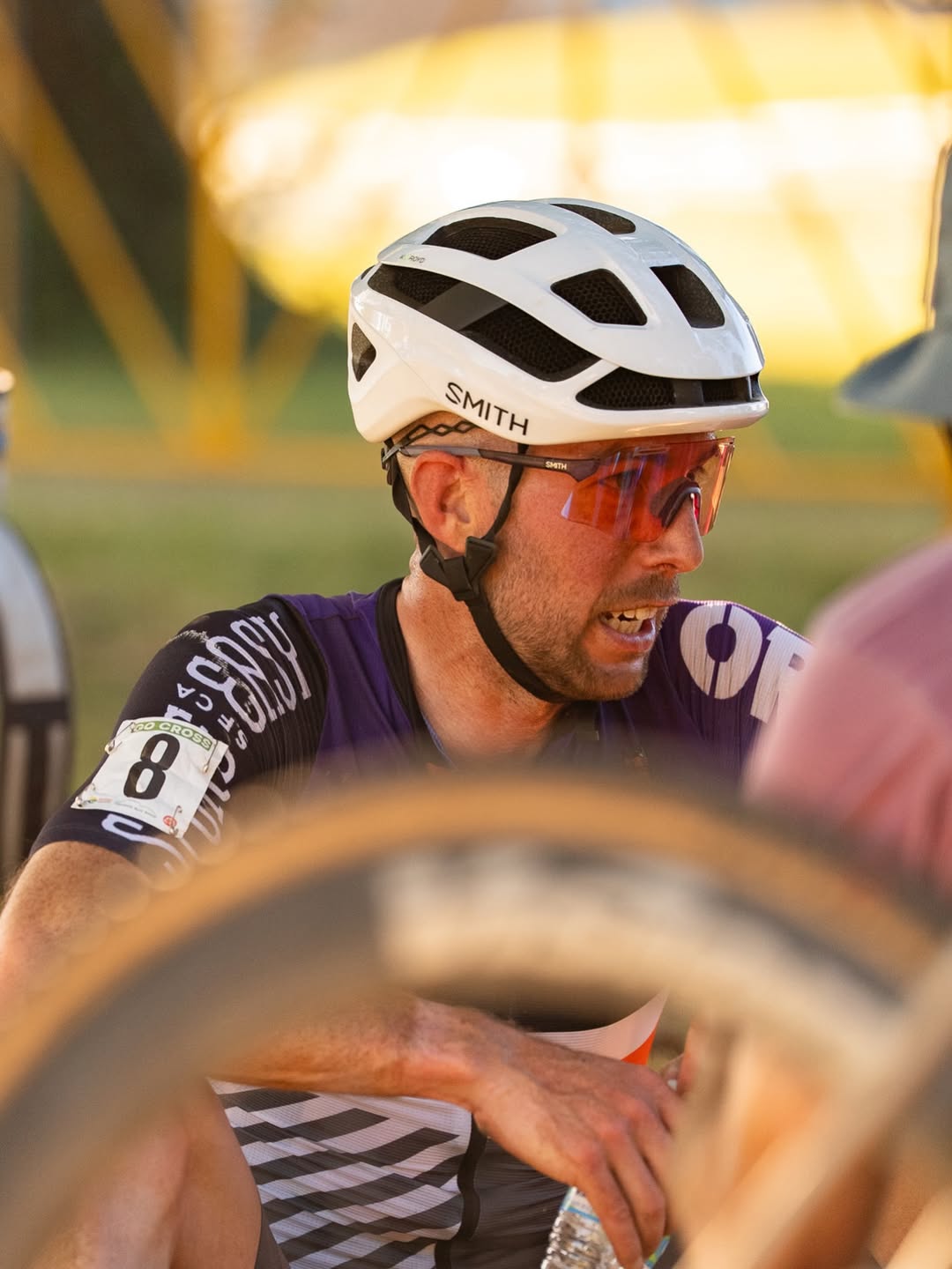 Ben Frederick in his cycling helmet and purple race jersey beside his bike.