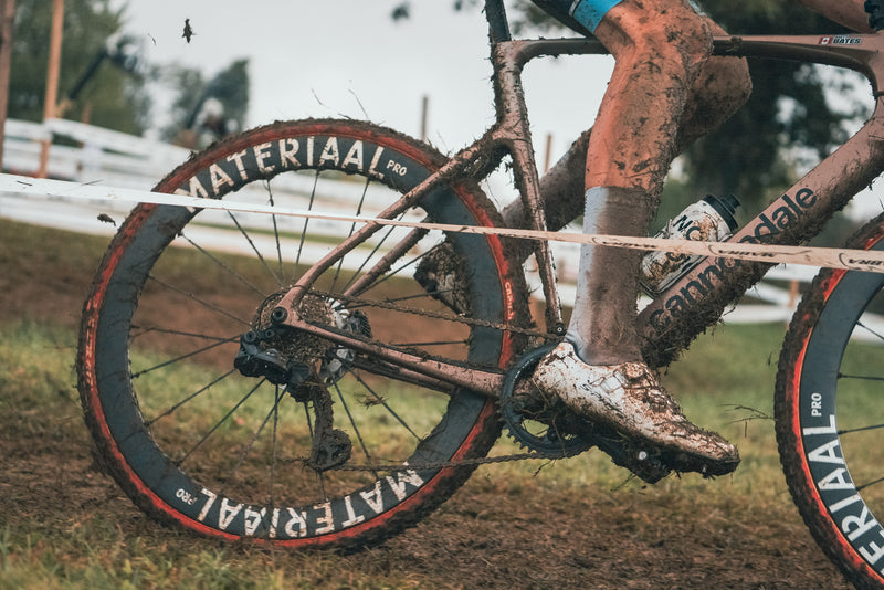 Materiaal carbon wheels racing through mud, with a close-up of the rear wheel and rider.